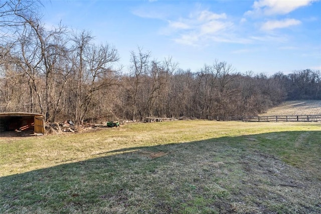 view of yard with a rural view, an outdoor structure, fence, and a forest view