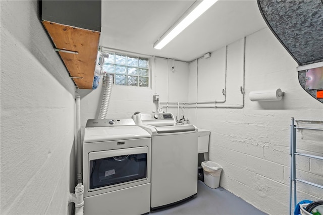 clothes washing area featuring concrete block wall, cabinet space, and washer and clothes dryer