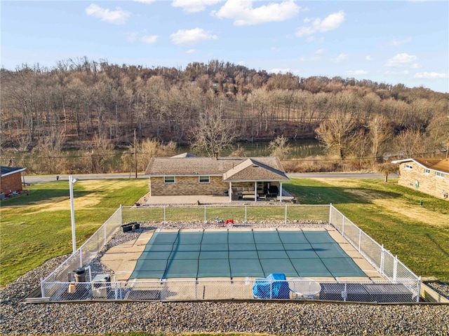 view of pool with fence, a fenced in pool, a wooded view, a yard, and a patio area