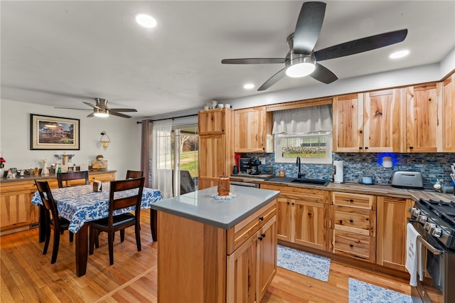 kitchen with light wood-type flooring, gas range oven, decorative backsplash, a ceiling fan, and a sink