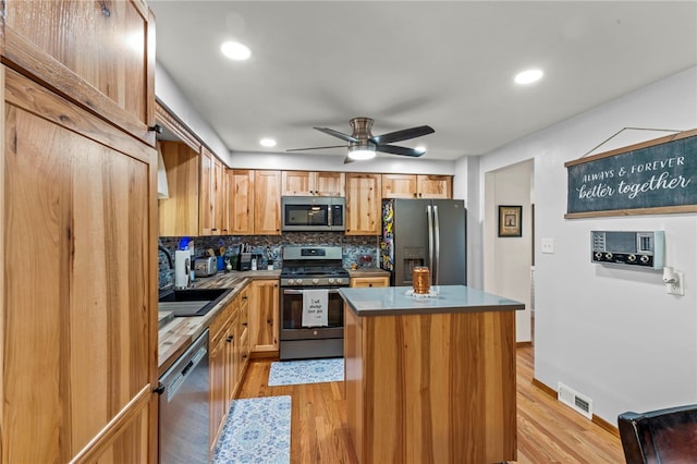 kitchen featuring light wood-type flooring, visible vents, a kitchen island, stainless steel appliances, and decorative backsplash