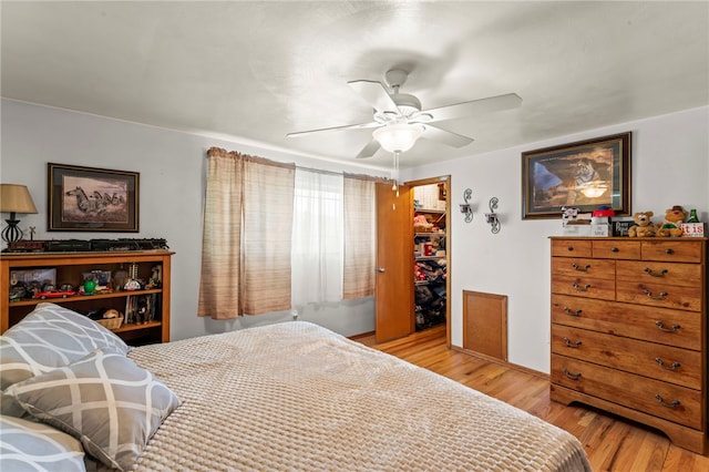 bedroom with a spacious closet, a closet, a ceiling fan, and light wood-style floors