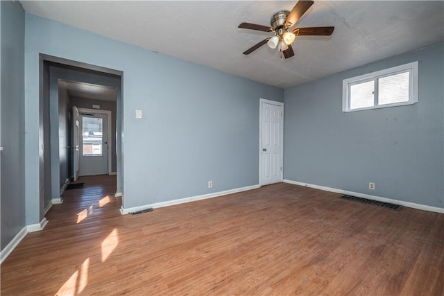 empty room featuring a ceiling fan, wood finished floors, visible vents, and baseboards