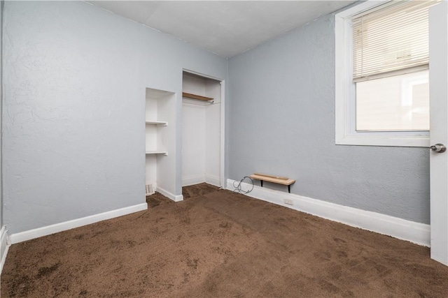 unfurnished bedroom with baseboards, carpet floors, a closet, and a textured wall