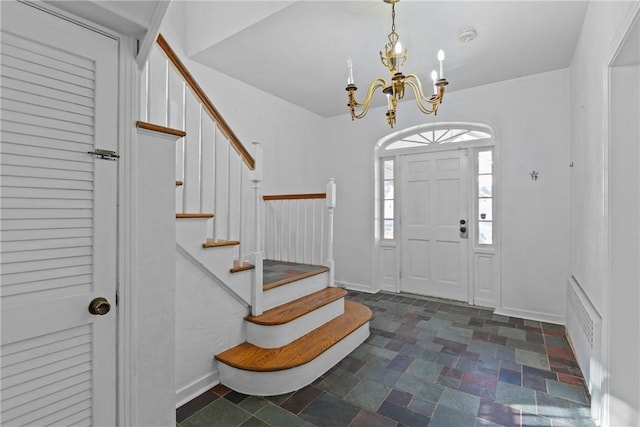 entrance foyer featuring stairway, baseboards, a notable chandelier, and stone finish flooring