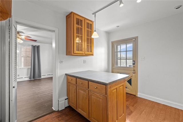 kitchen featuring a ceiling fan, dark wood finished floors, a peninsula, glass insert cabinets, and brown cabinets