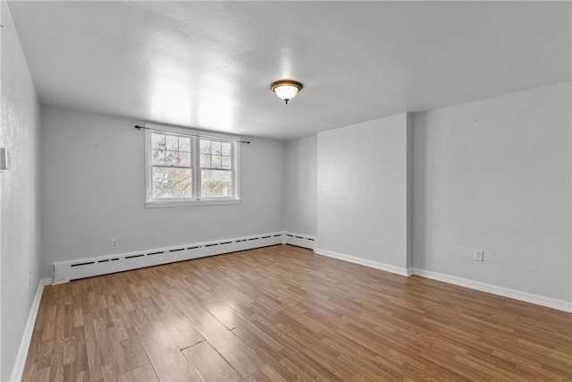 spare room featuring a baseboard heating unit, baseboards, and wood finished floors