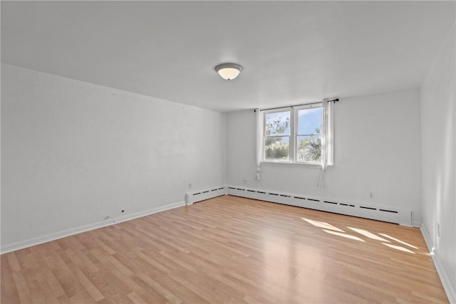 empty room featuring baseboards, light wood-type flooring, and a baseboard radiator