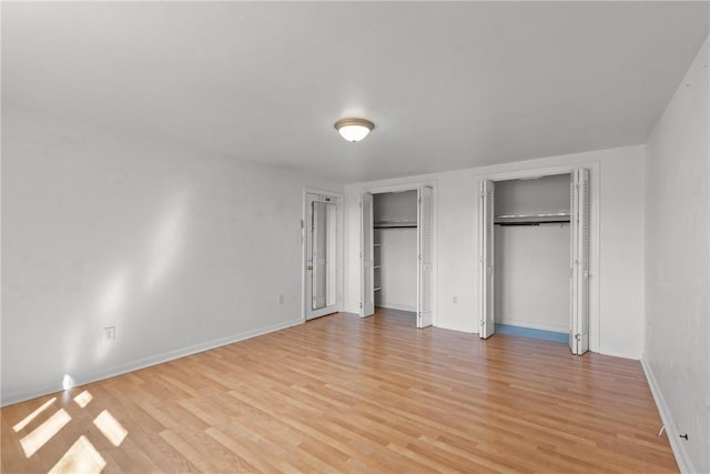 unfurnished bedroom with baseboards, light wood-type flooring, and two closets