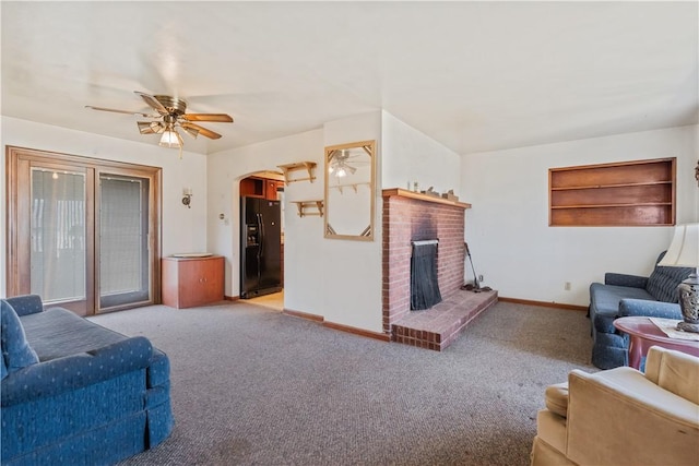 carpeted living area featuring baseboards, arched walkways, a fireplace, and a ceiling fan