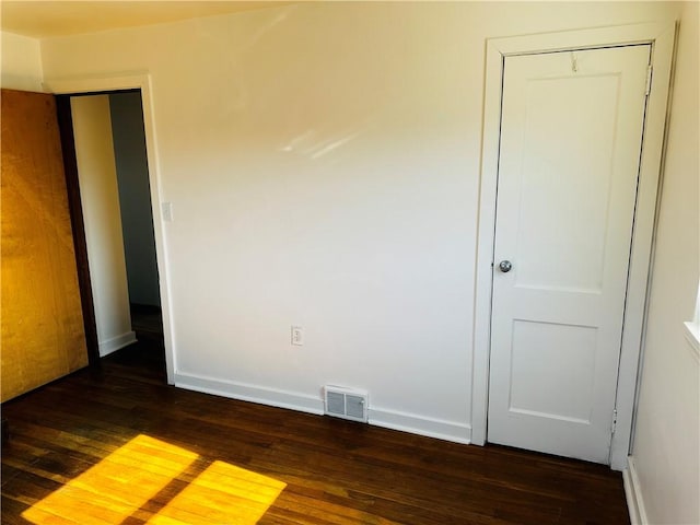 spare room with dark wood-style floors, visible vents, and baseboards