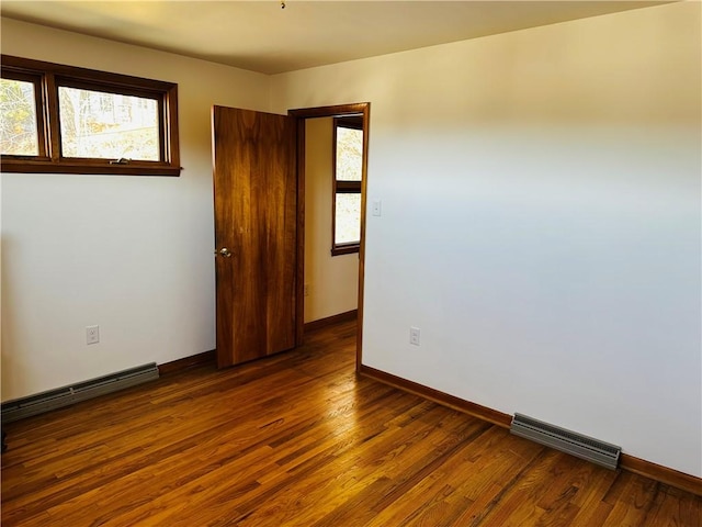 unfurnished room featuring visible vents, baseboards, wood finished floors, and a baseboard heating unit