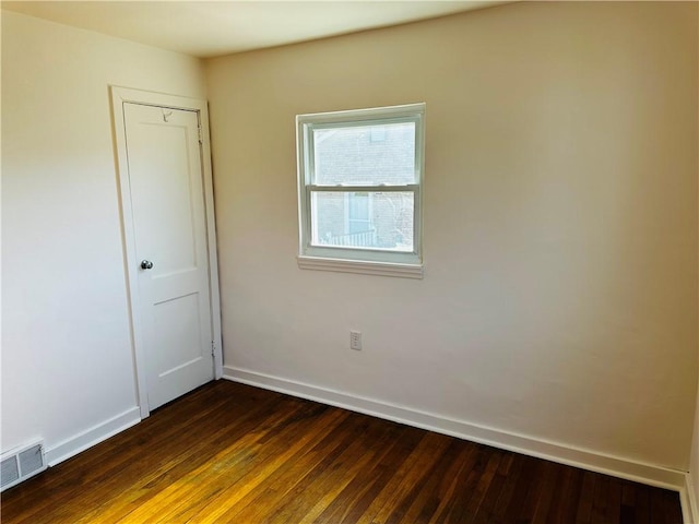 unfurnished room featuring dark wood-style floors, visible vents, and baseboards