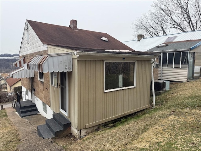 rear view of property with central air condition unit, entry steps, and a chimney