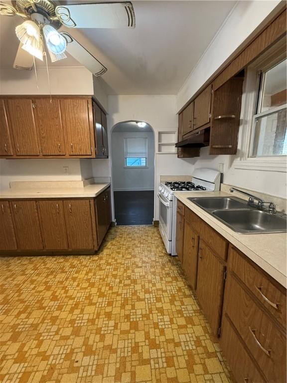 kitchen featuring under cabinet range hood, white gas range, arched walkways, a ceiling fan, and a sink