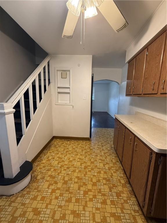 kitchen featuring arched walkways, baseboards, light countertops, and a ceiling fan