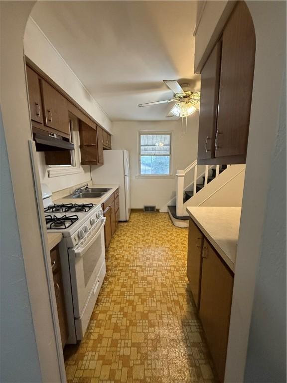 kitchen featuring a ceiling fan, under cabinet range hood, white appliances, arched walkways, and light countertops