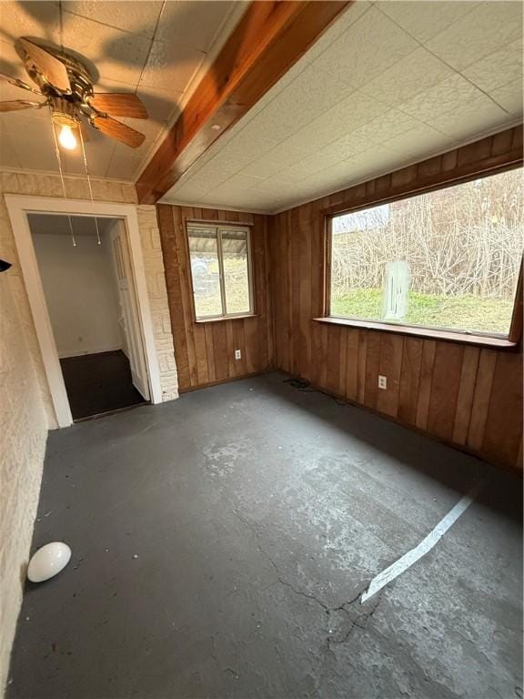 unfurnished room featuring concrete flooring, wood walls, and a ceiling fan