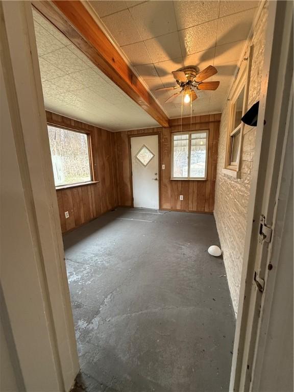 unfurnished living room with unfinished concrete floors, a drop ceiling, a ceiling fan, and wood walls