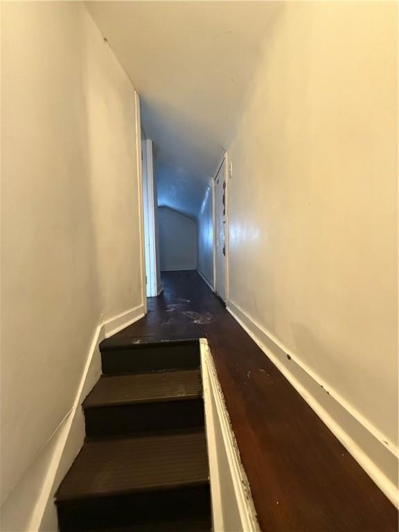 staircase featuring vaulted ceiling, wood finished floors, and baseboards