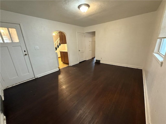 entrance foyer with baseboards, arched walkways, visible vents, and dark wood-style flooring