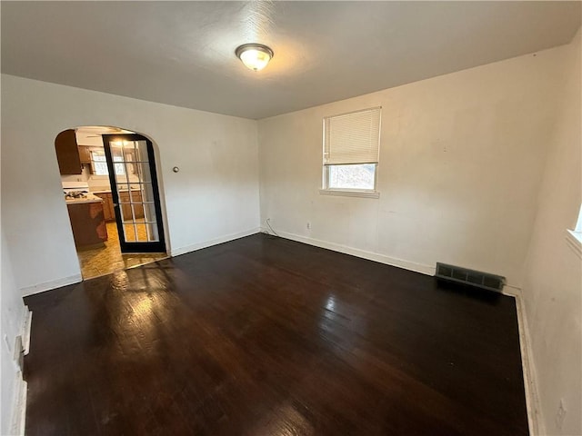 unfurnished room featuring arched walkways, visible vents, baseboards, and dark wood-style flooring