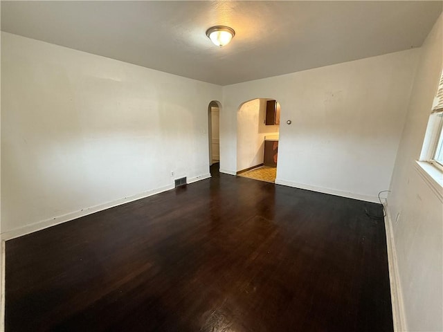 empty room with arched walkways, visible vents, dark wood finished floors, and baseboards