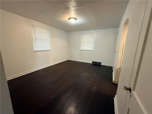 empty room featuring dark wood finished floors, visible vents, and baseboards