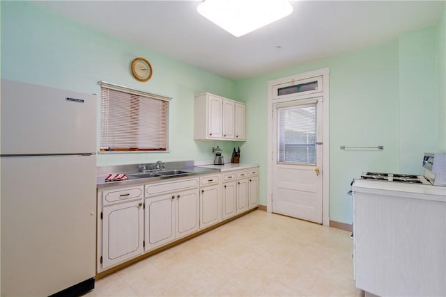 kitchen with light floors, baseboards, freestanding refrigerator, a sink, and light countertops