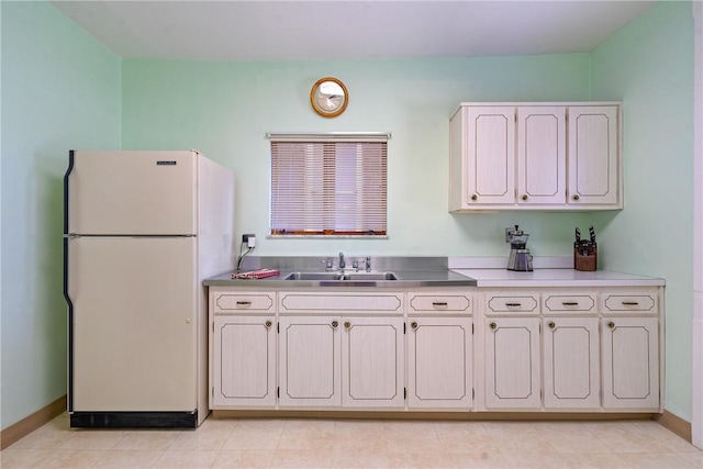 kitchen with light countertops, baseboards, freestanding refrigerator, and a sink