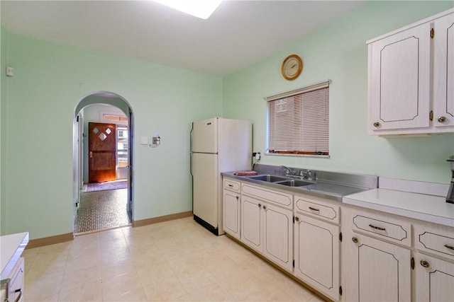 kitchen with baseboards, light countertops, freestanding refrigerator, arched walkways, and a sink