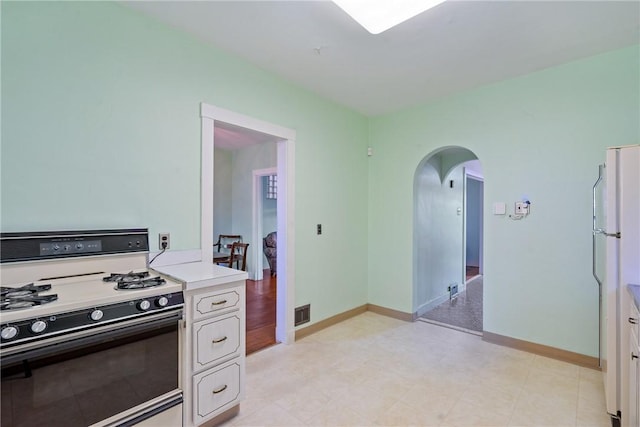 kitchen featuring baseboards, arched walkways, light countertops, gas range oven, and white cabinetry