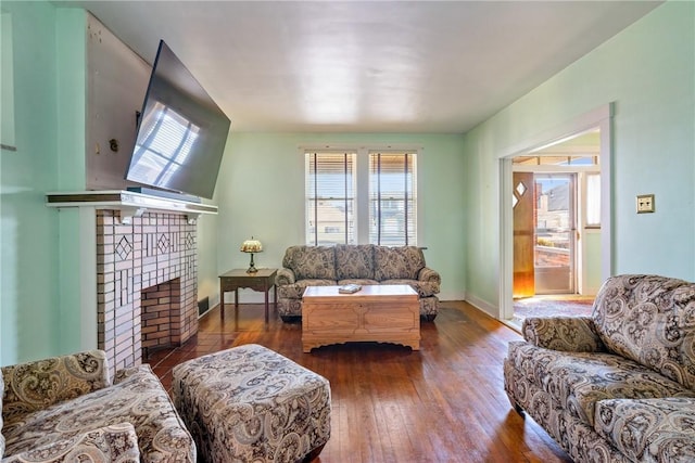 living area featuring a brick fireplace, baseboards, and hardwood / wood-style floors