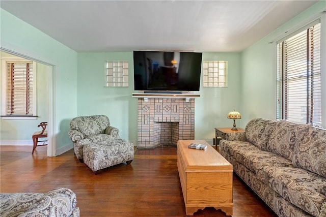 living room featuring a brick fireplace, baseboards, and dark wood-style flooring