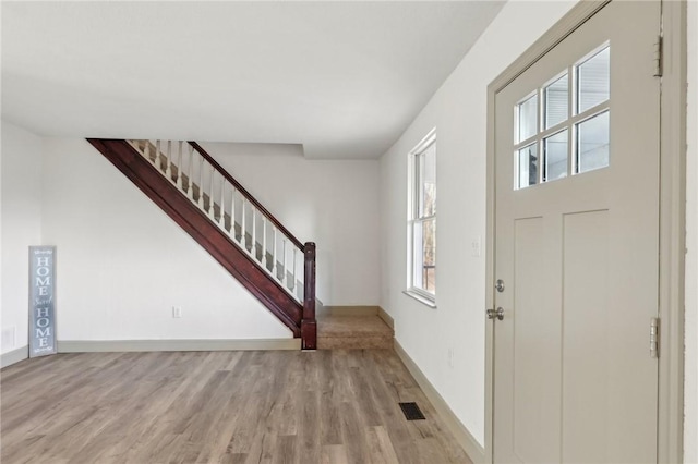 foyer entrance featuring visible vents, baseboards, light wood-style floors, and stairway