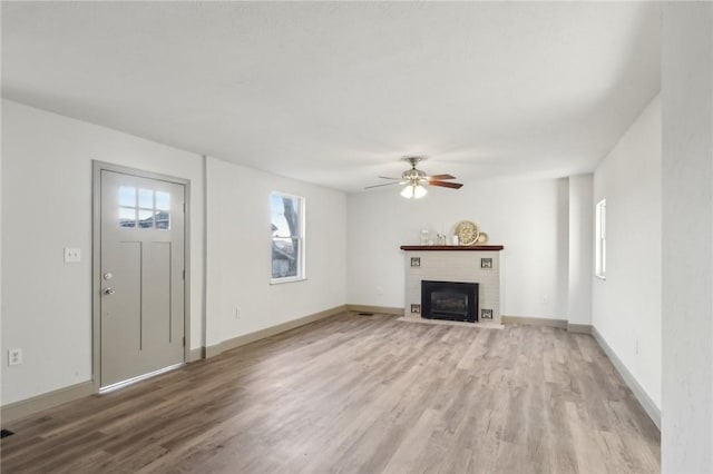 unfurnished living room with baseboards, a brick fireplace, light wood-style flooring, and a ceiling fan