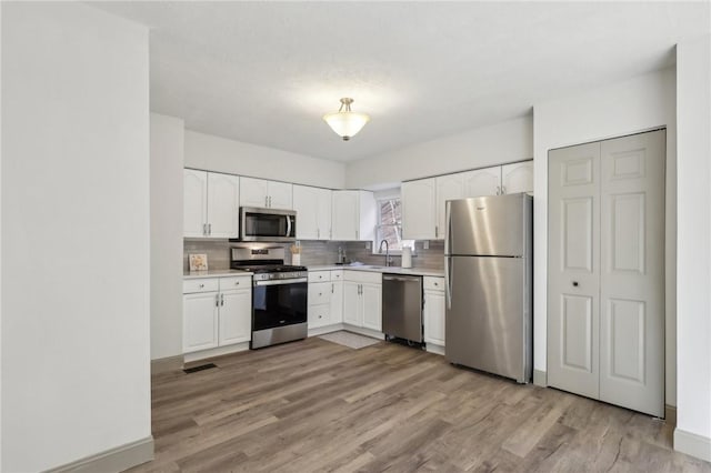 kitchen featuring light countertops, decorative backsplash, appliances with stainless steel finishes, light wood-style floors, and a sink