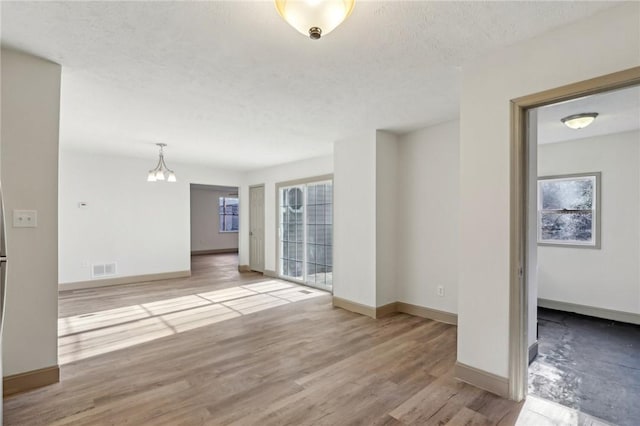 spare room with visible vents, baseboards, a chandelier, wood finished floors, and a textured ceiling