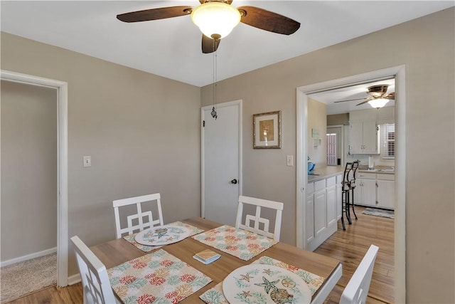 dining space featuring light wood finished floors, baseboards, and a ceiling fan