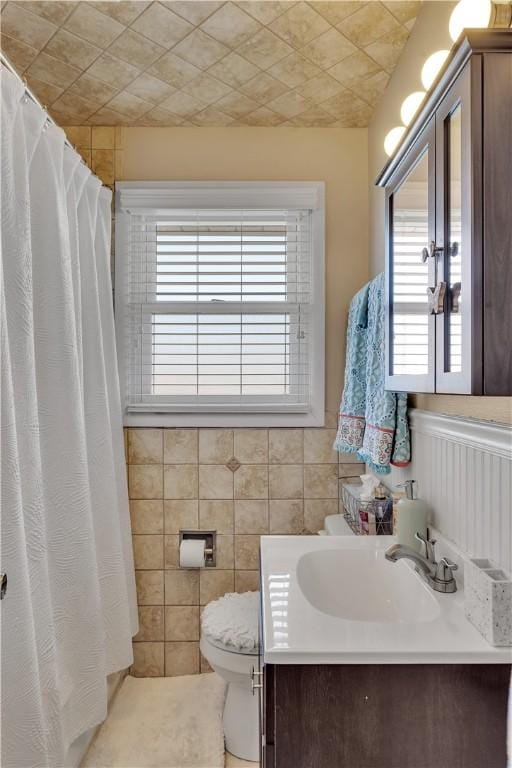 bathroom featuring a wealth of natural light, a wainscoted wall, toilet, and vanity