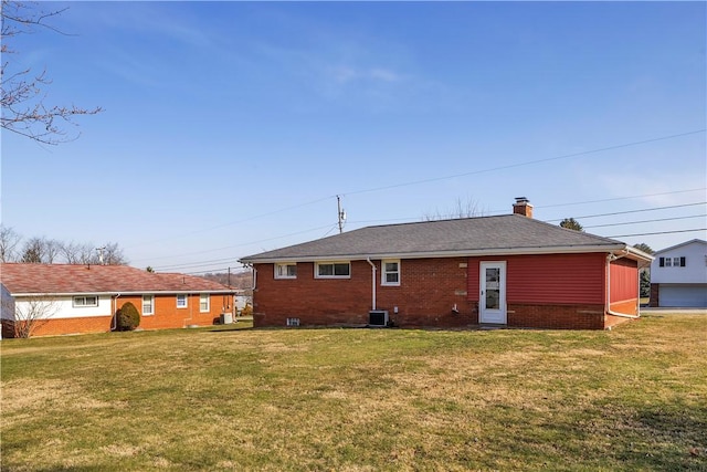 rear view of house with central AC unit, roof with shingles, a yard, a chimney, and brick siding