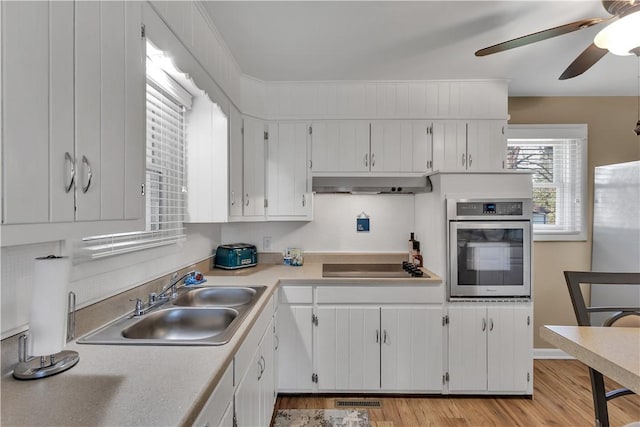 kitchen with a ceiling fan, a sink, wall chimney exhaust hood, stainless steel oven, and black electric cooktop