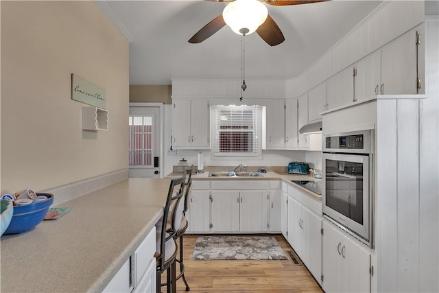 kitchen with under cabinet range hood, oven, light countertops, and a sink