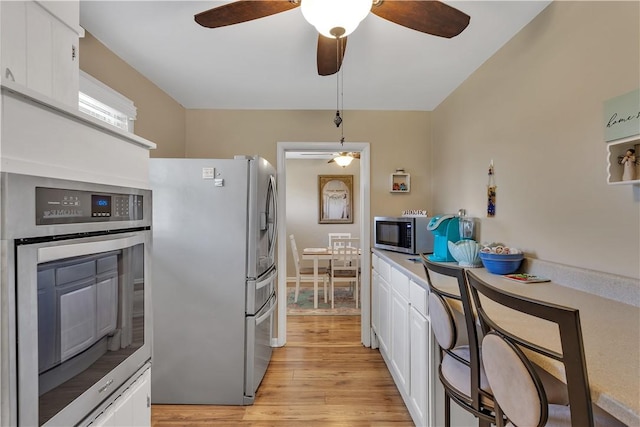 kitchen with light wood-style flooring, ceiling fan, stainless steel appliances, light countertops, and white cabinets