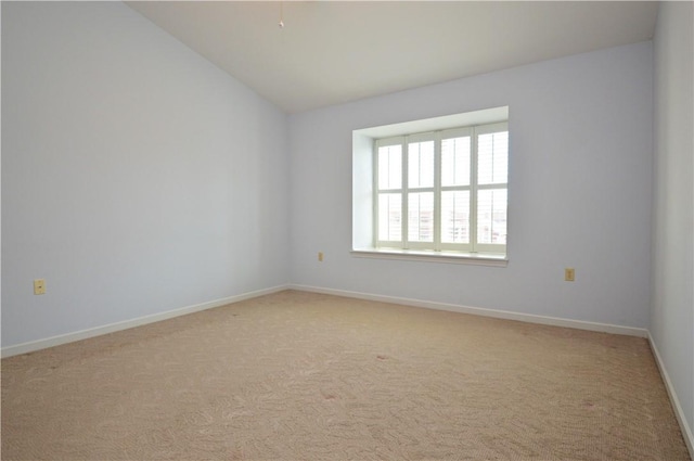 empty room with vaulted ceiling, light colored carpet, and baseboards