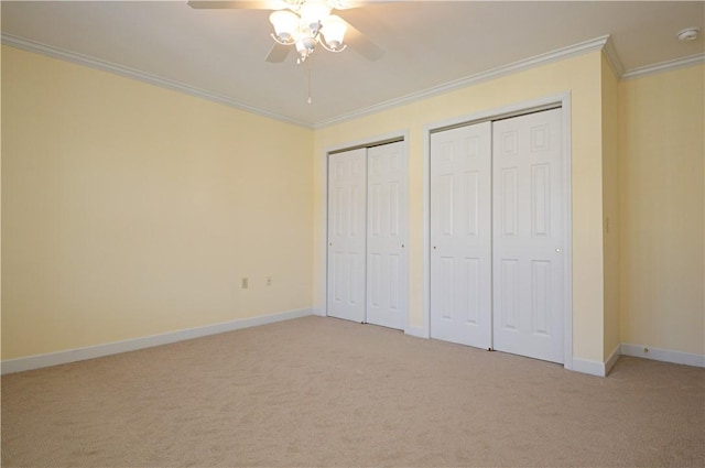 unfurnished bedroom featuring light colored carpet, two closets, crown molding, and baseboards