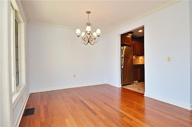 unfurnished room with baseboards, visible vents, light wood finished floors, ornamental molding, and a notable chandelier