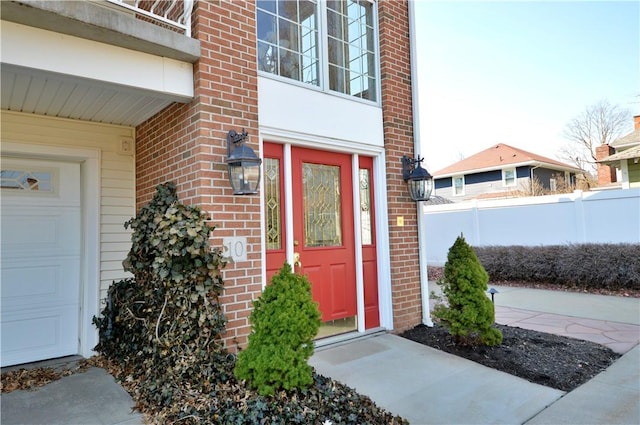 property entrance with a garage, fence, and brick siding