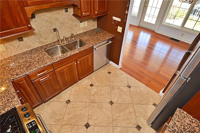 kitchen featuring tasteful backsplash, visible vents, stone counters, stainless steel dishwasher, and a sink