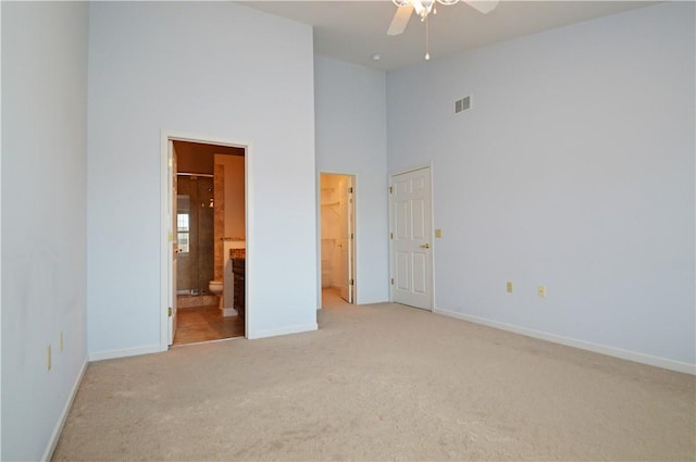 unfurnished bedroom with visible vents, light colored carpet, ensuite bathroom, and a towering ceiling